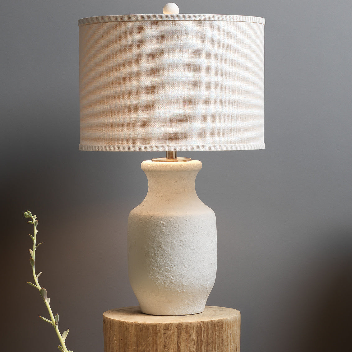 White cement table lamp with white shade on wooden side table.