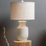 White cement table lamp with white shade on wooden side table.