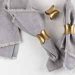 Gold scallop napkin rings on grey napkins on white table.