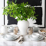 White dishes on plaid tablecloth with black and white artwork behind on white wall