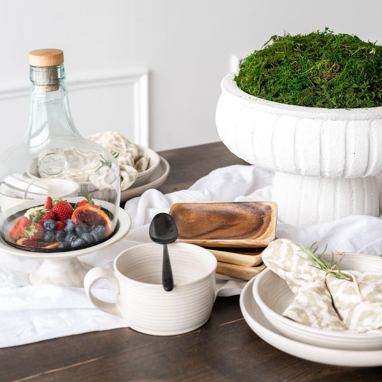 glass cloche with copper rim bottom and wine cork stopper  covering fruit on white pedestal on wood table
