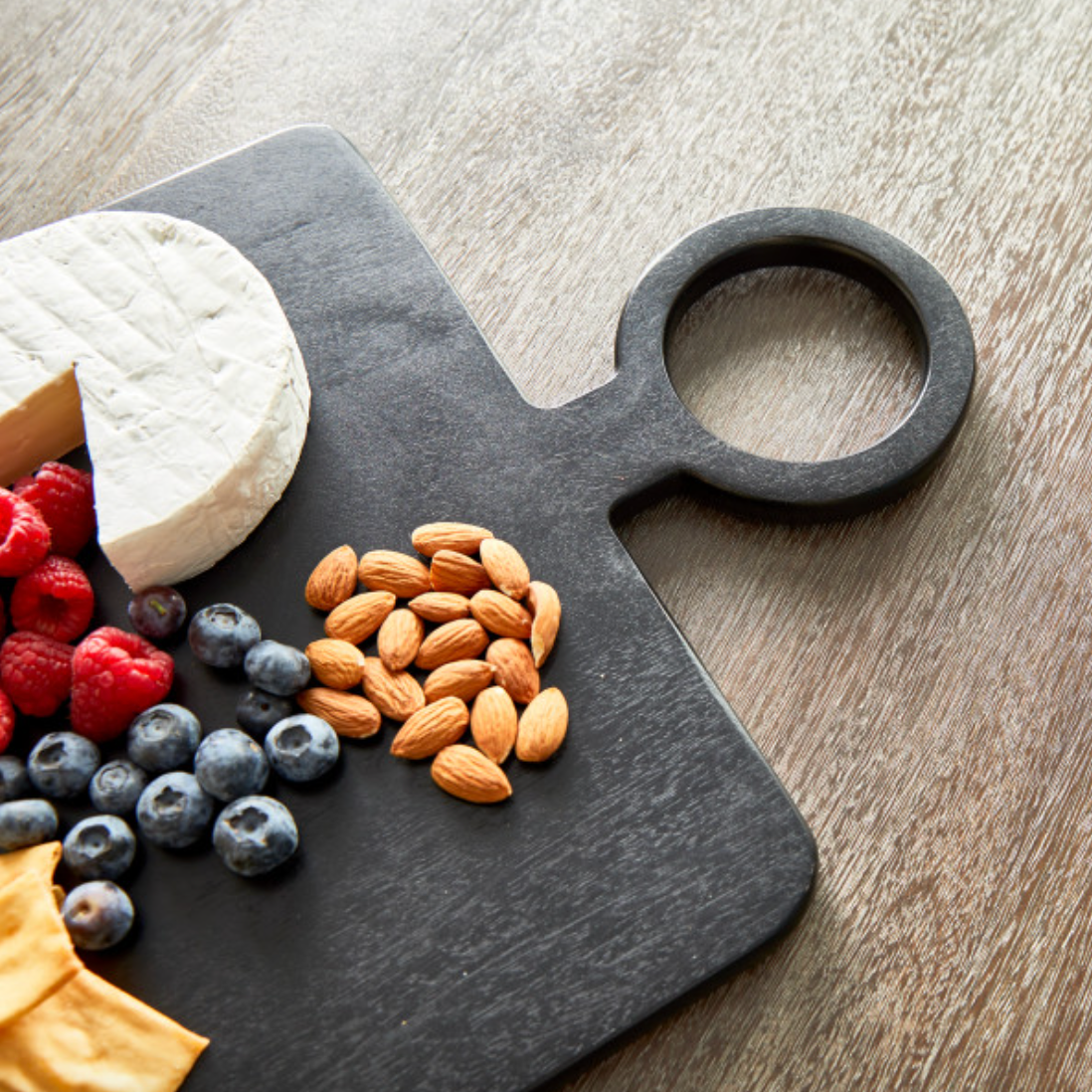 Black Nox serving board on wood table with fruit and nuts 