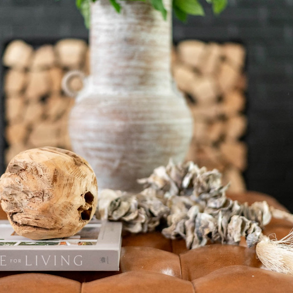 oyster shell decor garland on leather ottoman with wood orb and vase in the background with a terracotta vase in the background