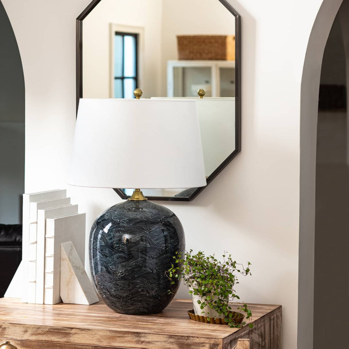 Harbor ceramic lamp on wood table in front of black mirror on white wall.