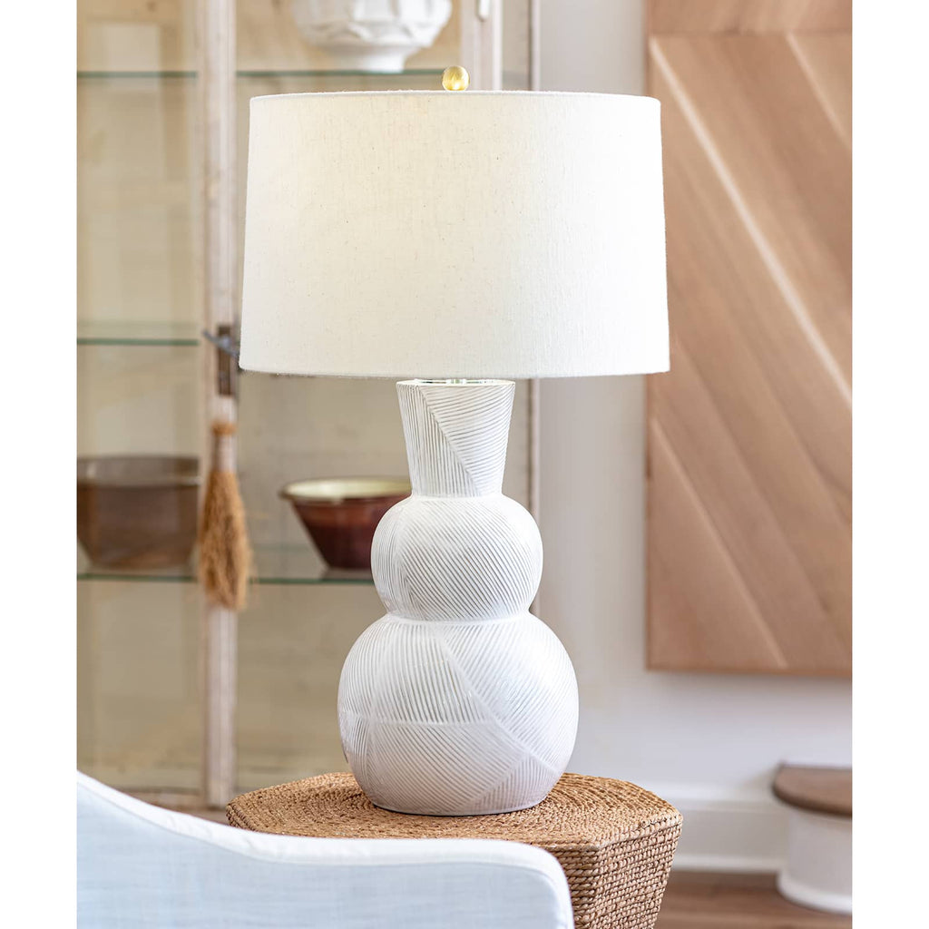 White hugo ceramic lamp on wood side table in room with furniture.