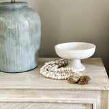 Aqua table lamp on tan nightstand in bedroom with white wall.