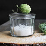 pressed glass salt cellar with salt inside sitting on a wood board